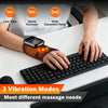 A hand wearing a heated vibration wrist brace massager is shown resting on a laptop keyboard.
