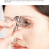 A hand is using a clear dual-type eyelash curler with a comb to curl eyelashes on a woman's eye.