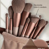 A collection of professional makeup brushes in various shades of rose gold and nude tones, shown inside a fabric pouch.