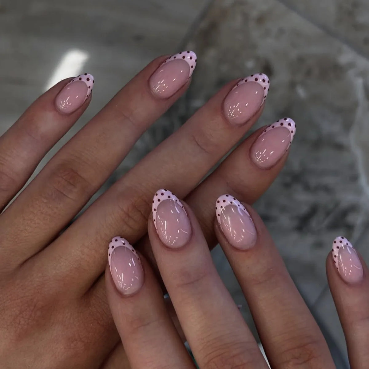 Une main montrant un ensemble de faux ongles press-on roses à l'amande française avec de petits pois blancs.