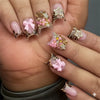A hand displays a set of nude pink press-on nails featuring leopard print accents and 3D floral charms.