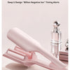 A pink waver curling iron is shown on a white surface next to a glass bottle.