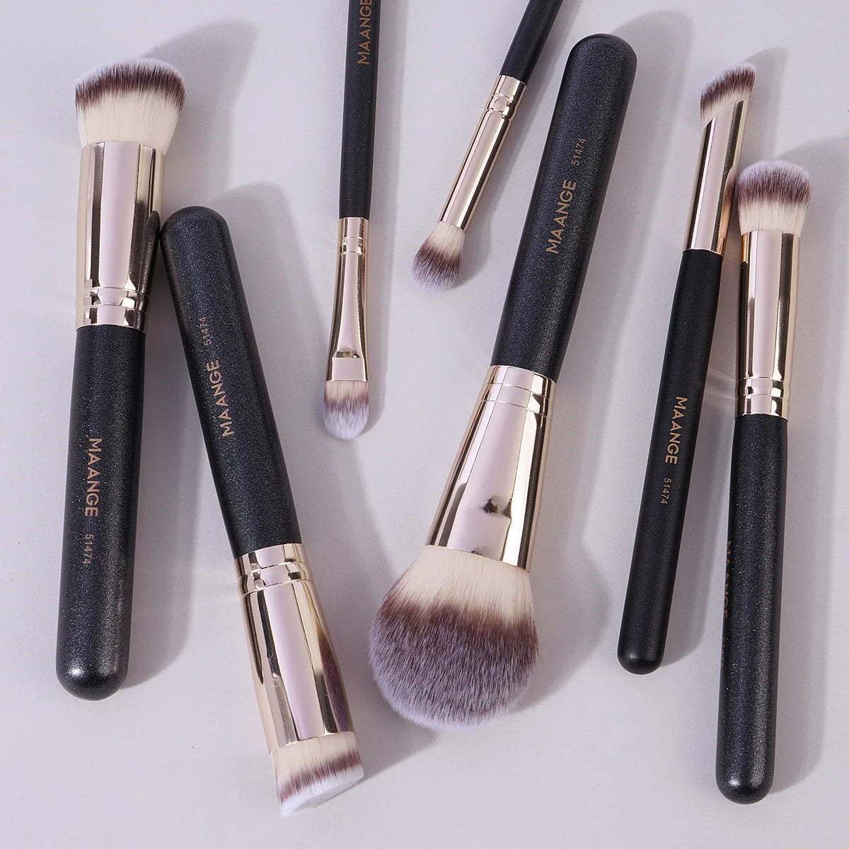 A set of seven professional makeup brushes with black handles and gold accents, including various sizes and shapes.