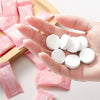 A hand holds several white disposable wet wipes on a wooden surface.