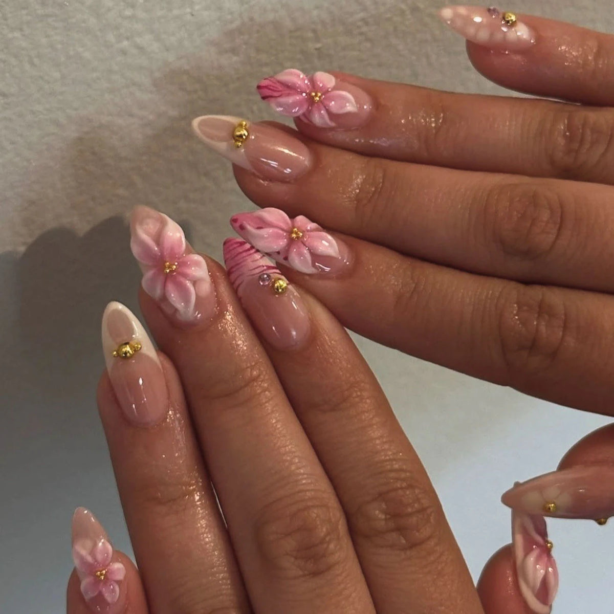 Gros plan sur des mains montrant un ensemble de faux ongles à pincement roses français avec de petits accents dorés.