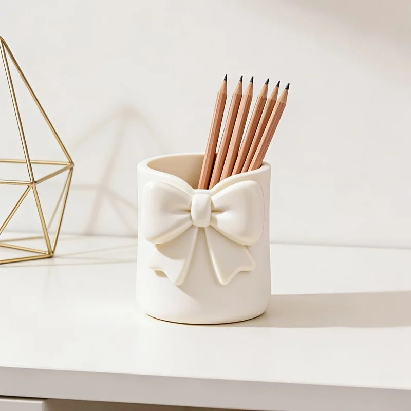 Un organisateur de rangement en céramique blanche contient un paquet de crayons en bois et un support géométrique doré sur un