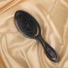 Peigne noir polyvalent mouillé et sec avec poignée flexible sur fond de tissu beige fluide.