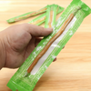 Une main tient une brosse à dents naturelle miswak emballée dans un emballage vert sur une surface en bois.