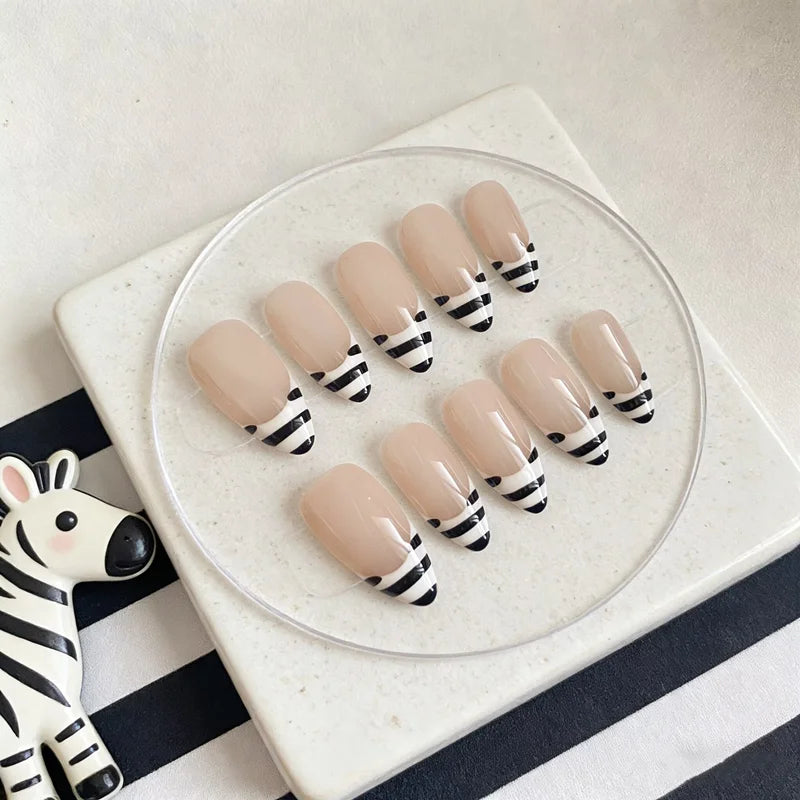 Un set de uñas postizas con rayas de cebra beige y negro, exhibidas en una placa de vidrio transparente sobre una superficie 