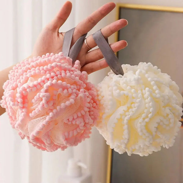 Una mano sostiene dos esponjas de baño suaves de malla rosa y blanca para exfoliación corporal suave