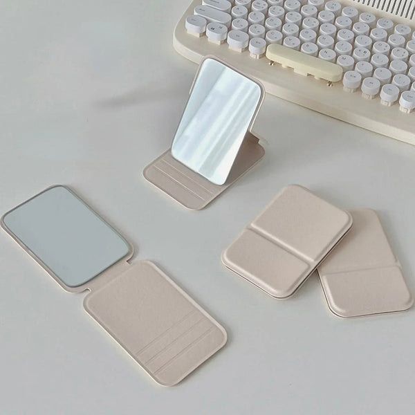 A portable makeup mirror with a light-colored PU leather casing and a reflective surface is shown next to a keyboard.