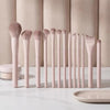 A set of professional loose powder makeup brushes in a pale pink color arranged in a row on a white marble surface.