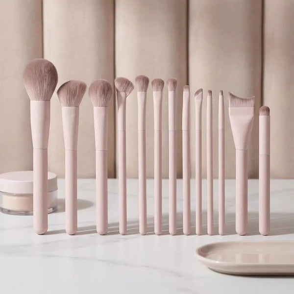 A set of professional loose powder makeup brushes in a pale pink color arranged in a row on a white surface.