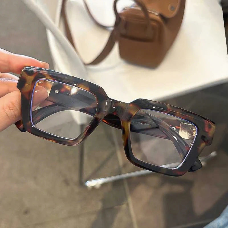 Une paire de lunettes à monture carrée rétro écaille de tortue posées sur une surface blanche.