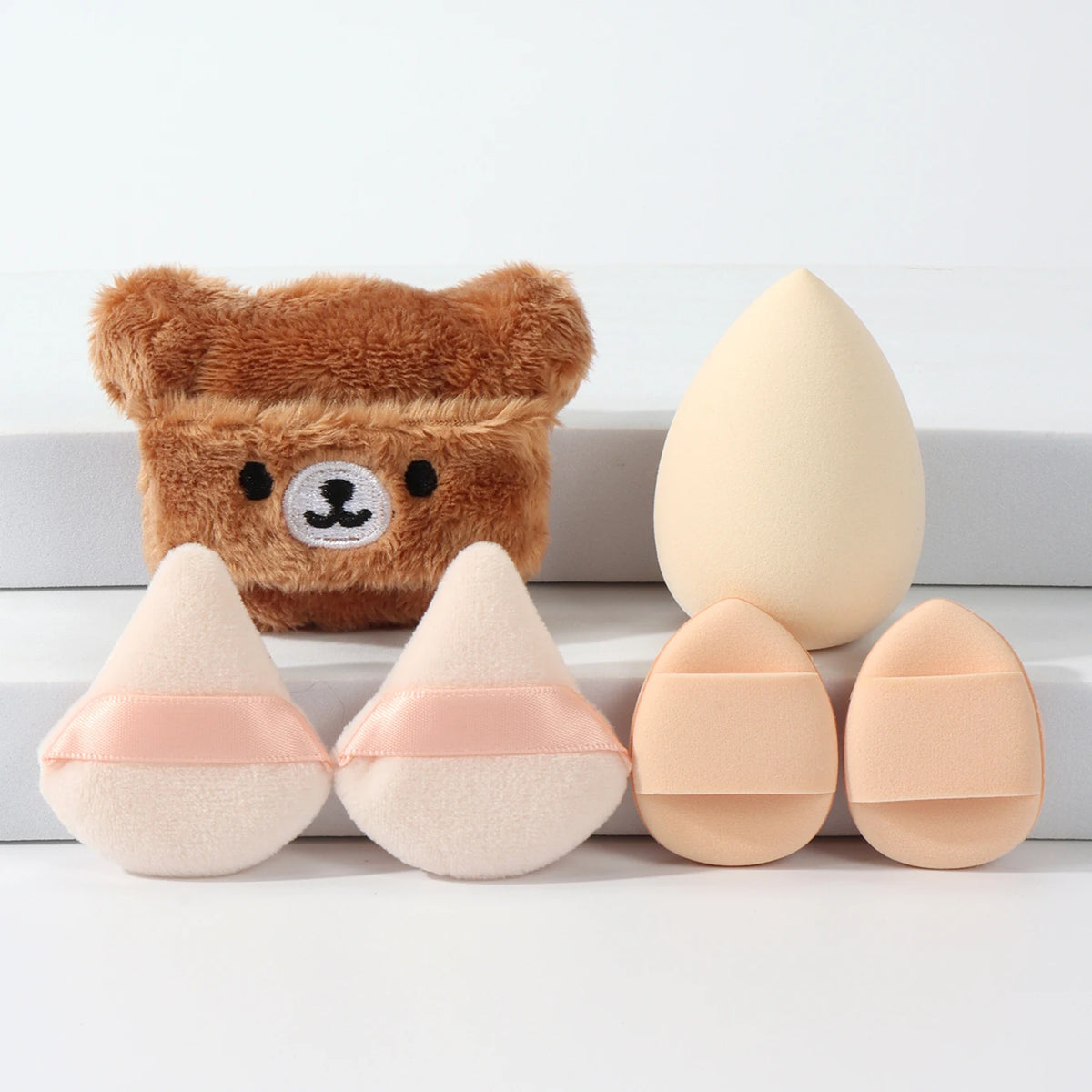 Un ensemble de poudre compacte avec des applicateurs en forme d'ours et plusieurs poudres ovales dans des tons nude.