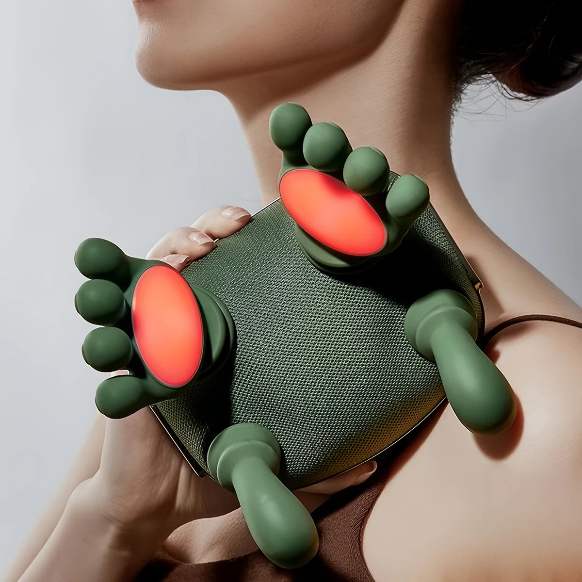 A hand is holding a green silicone massager with orange tips, demonstrating its use for neck and shoulder relief.