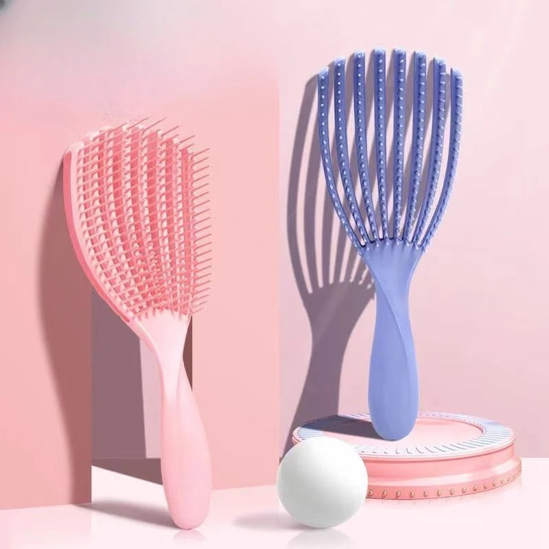 A pink massage detangler hair brush is shown next to a blue one and a pink silicone roller on a light pink background.