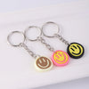 A set of yellow and pink cartoon smile face keychains hanging from metal rings on a white rectangular surface.