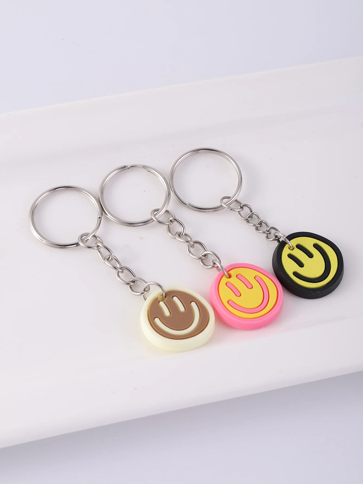 A set of yellow and pink cartoon smile face keychains hanging from metal rings on a white rectangular surface.