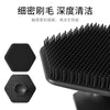A black silicone facial cleaning brush with multiple bristles shown alongside its detached head.