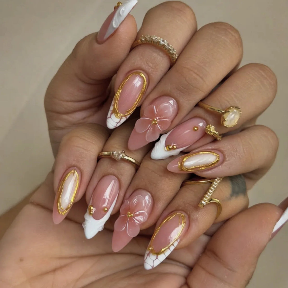 Une main montre des kits de vernis à poser en forme de fleur d'amande, avec des designs roses et blancs transparents et des a