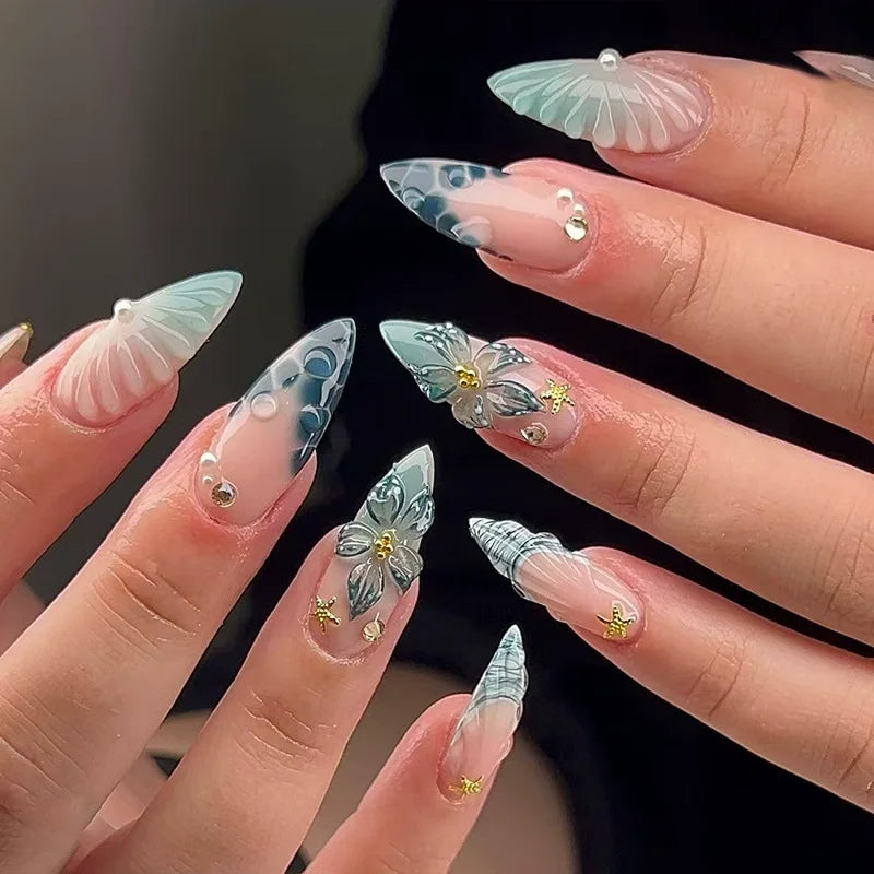 A close-up of ten manicured fingers displaying pink flower almond press on nails with iridescent and gold accents.