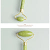 A gold-toned jade gua sha tool with a light green handle and oval stone, displayed against a light gray background.