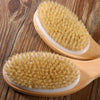 A natural wooden body brush with golden bristles is shown on a wooden surface.