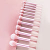 A collection of pink makeup brushes and puffs arranged in a diagonal line on a light background.