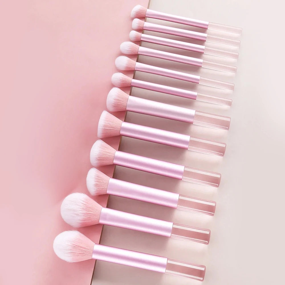 A collection of pink makeup brushes and puffs arranged in a diagonal line on a light background.