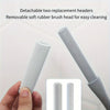A hand holds a long-handled manual foot scrubber with detachable replacement heads for cleaning.