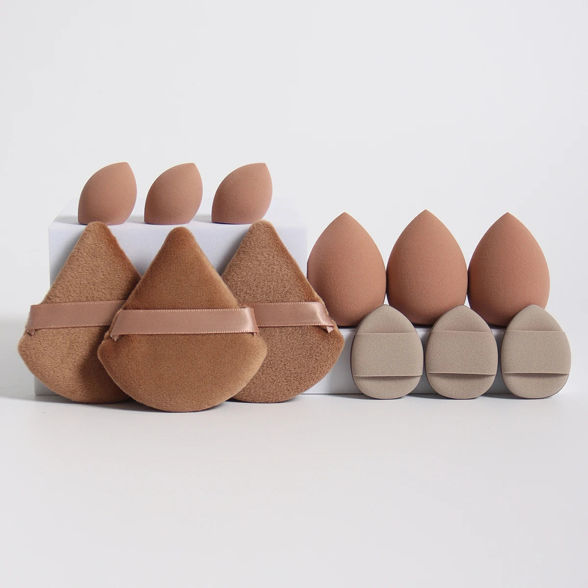 A set of twelve makeup sponges in various shades of nude and tan, arranged in a row.
