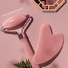 A pink jade gua sha tool is shown next to a hexagonal wooden mold and some green fern leaves.