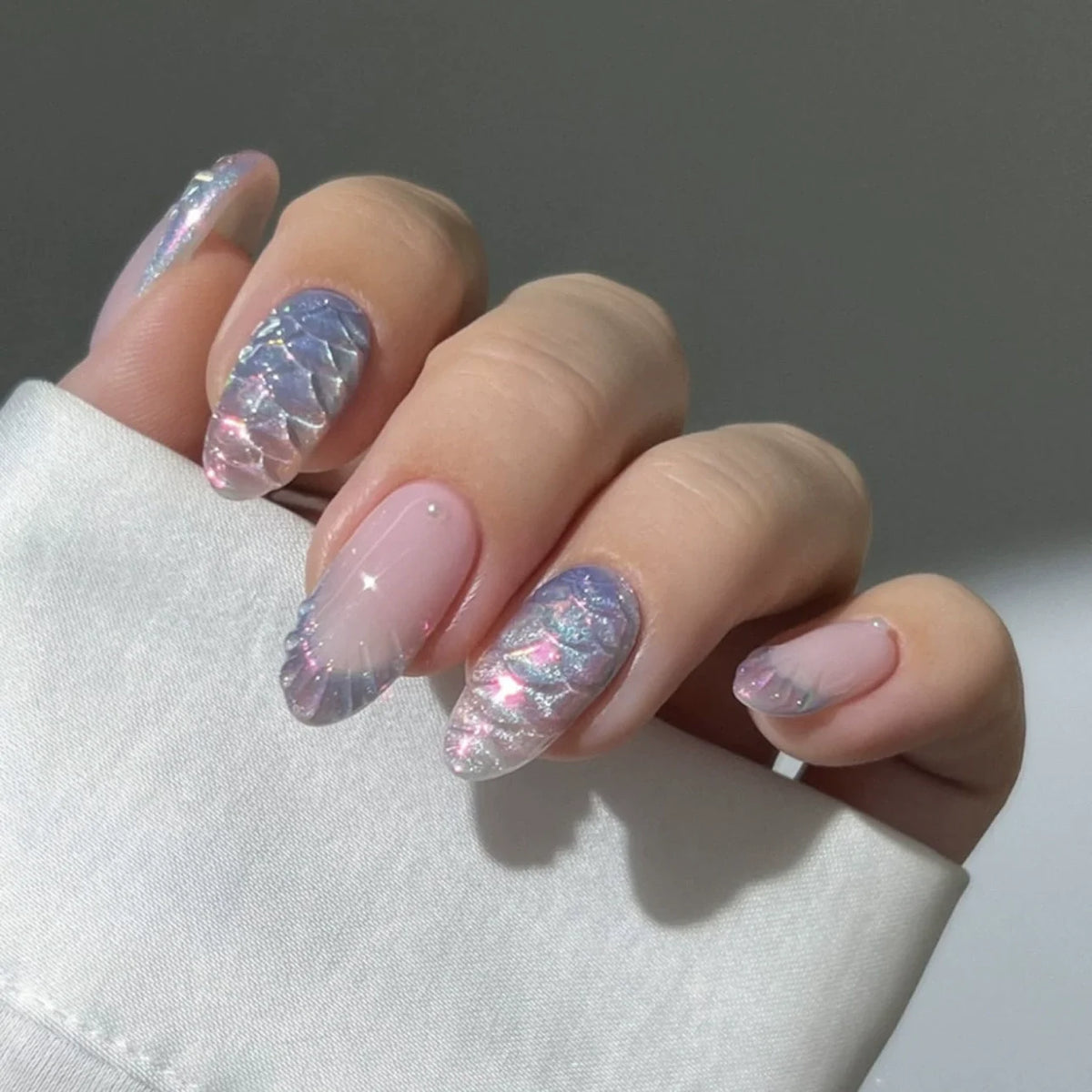A hand displaying 24 pink flower almond press on nails with a shimmering iridescent finish.