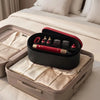 A black storage box containing a red hair styling tool and accessories, resting on a white bed.