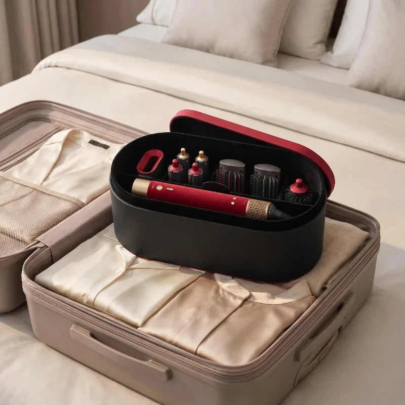 A black storage box containing a red hair styling tool and accessories, resting on a white bed.