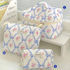 A quilted cotton makeup bag in white with blue and pink floral patterns is displayed on a white shelf.