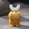 A yellow electric toothbrush for kids with a clear silicone brush head is shown against a gray, textured background.