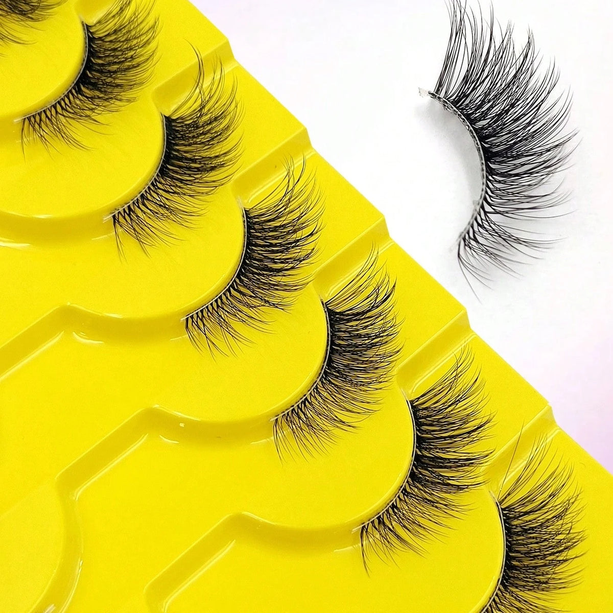 A close-up of yellow false eyelash pads with several pairs of wispy black lashes displayed on a white background.