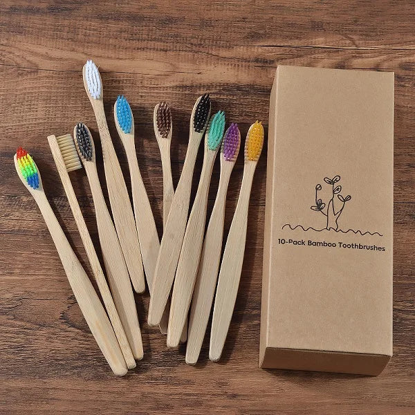 Une boîte contenant un pack de 10 brosses à dents en bambou, à côté de plusieurs brosses individuelles sur une surface en boi