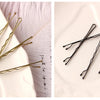 A collection of metal U-shaped hair pins in gold and black are displayed on a white plate.