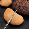 A titanium keychain toothpick set with a pointed tip resting on a light brown food item next to a dark brown porous object.