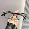 Une main tient une paire de lunettes à monture de chat avec des accents dorés sur un fond clair.