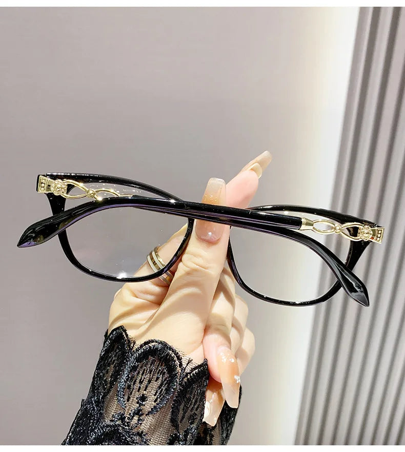 Une main tient une paire de lunettes à monture de chat avec des accents dorés sur un fond clair.