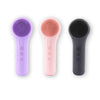 Three sonic facial cleansing brushes in purple, pink, and black with interchangeable silicone heads.