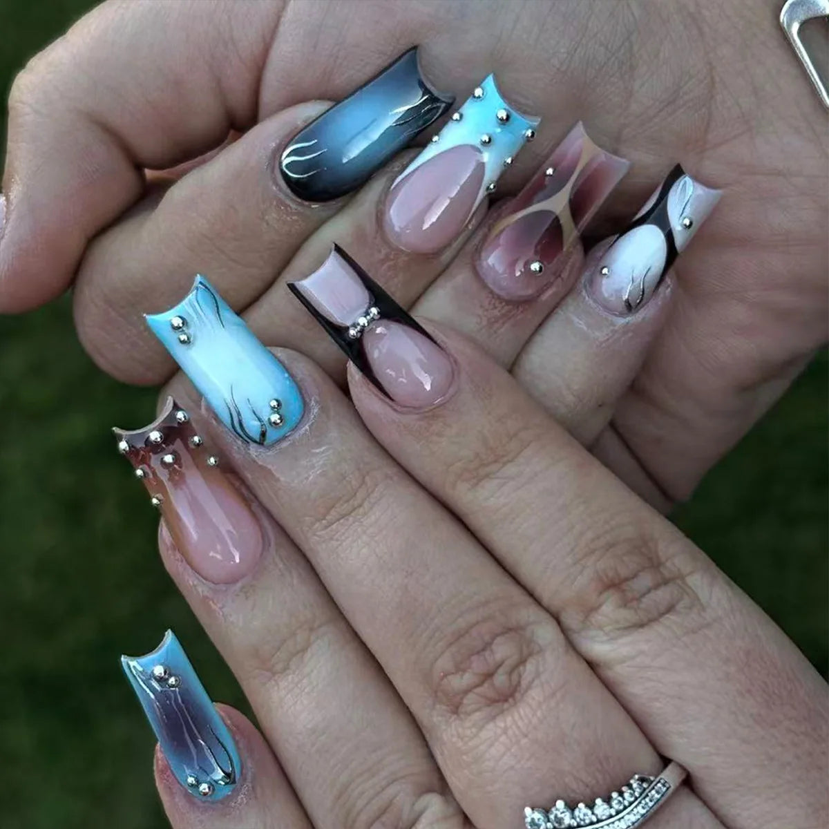 A hand displays a set of gothic Y2K press-on nails featuring iridescent blue and silver designs.