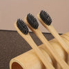 A set of six bamboo toothbrushes with black bristles are shown resting on a wooden cylinder.