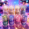 Une collection de bâtons de paillettes de diverses couleurs et textures, présentés sur une surface violette scintillante.