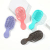 A collection of four mini travel hair brushes in pink, teal, purple, and gray are displayed on a white background.