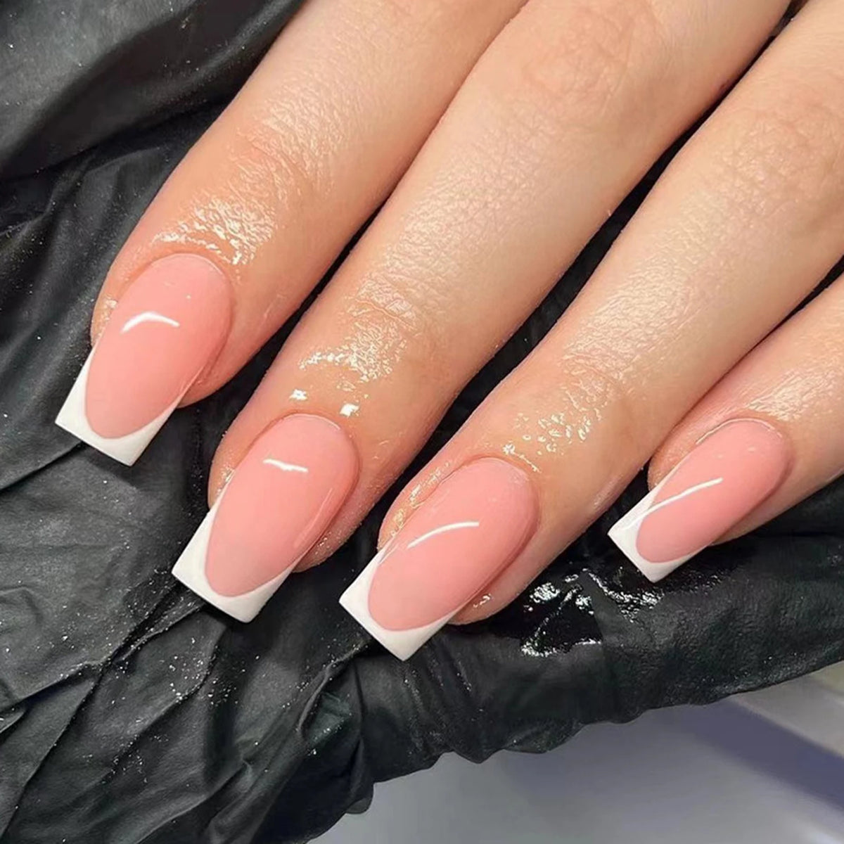 A close-up of ten manicured fingers displaying white French style coffin shaped press-on nails on a black background.